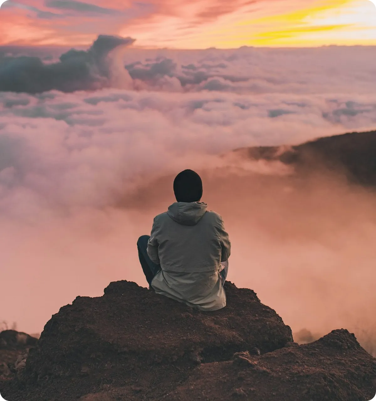 Person sitting peacefully on mountain rock above clouds at sunset - mental health wellness and therapy in Virginia Beach